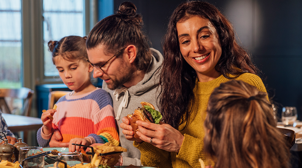 A family of four, parents and their two daughters, shared laughter and burgers at a lively restaurant